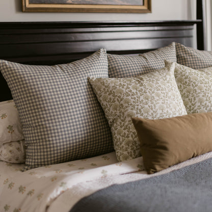 Dusty blue and white gingham patterned pillow displayed on a bed with coordinating decorative pillows.