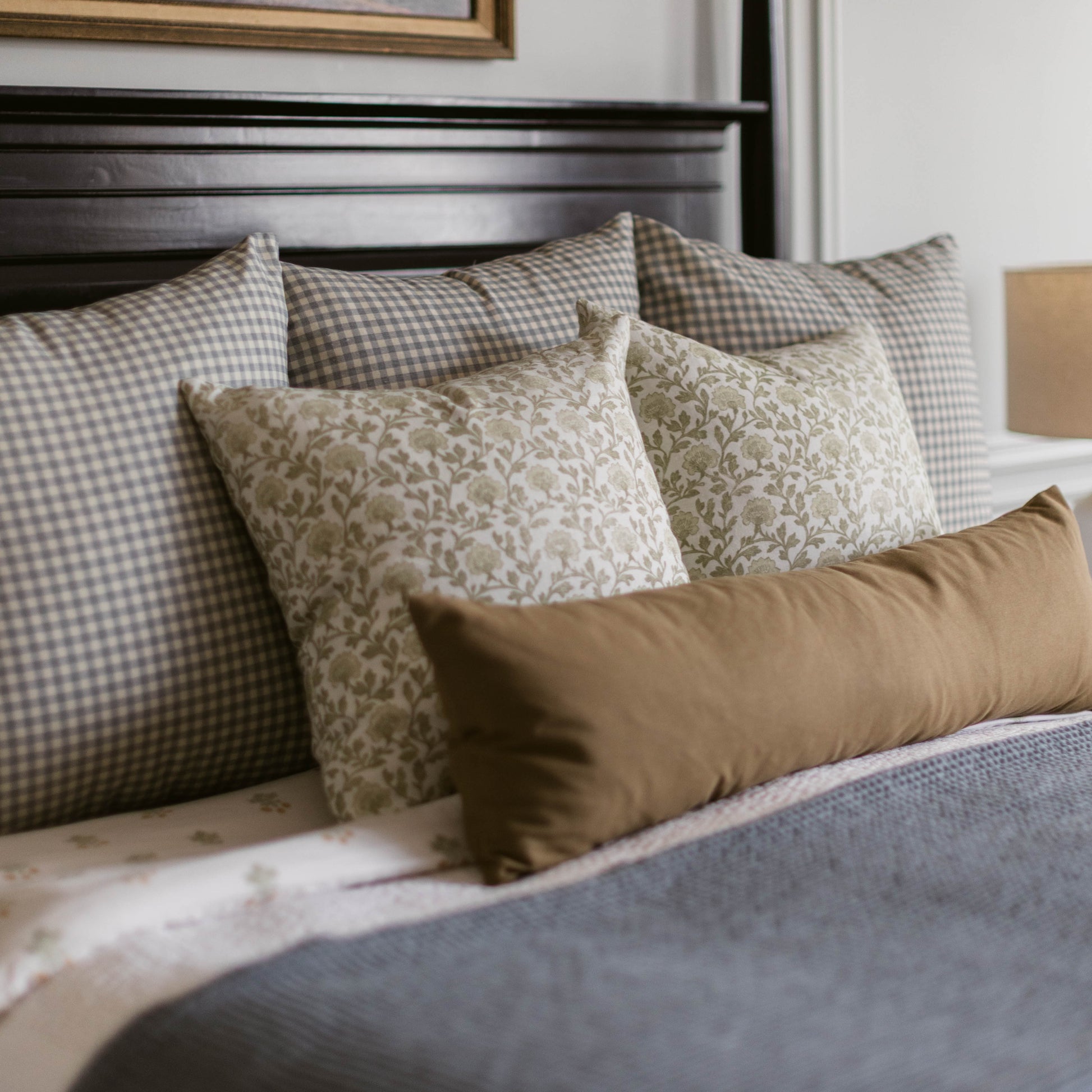 Rectangular linen pillow in taupe arranged among gingham and patterned pillows on a bed.