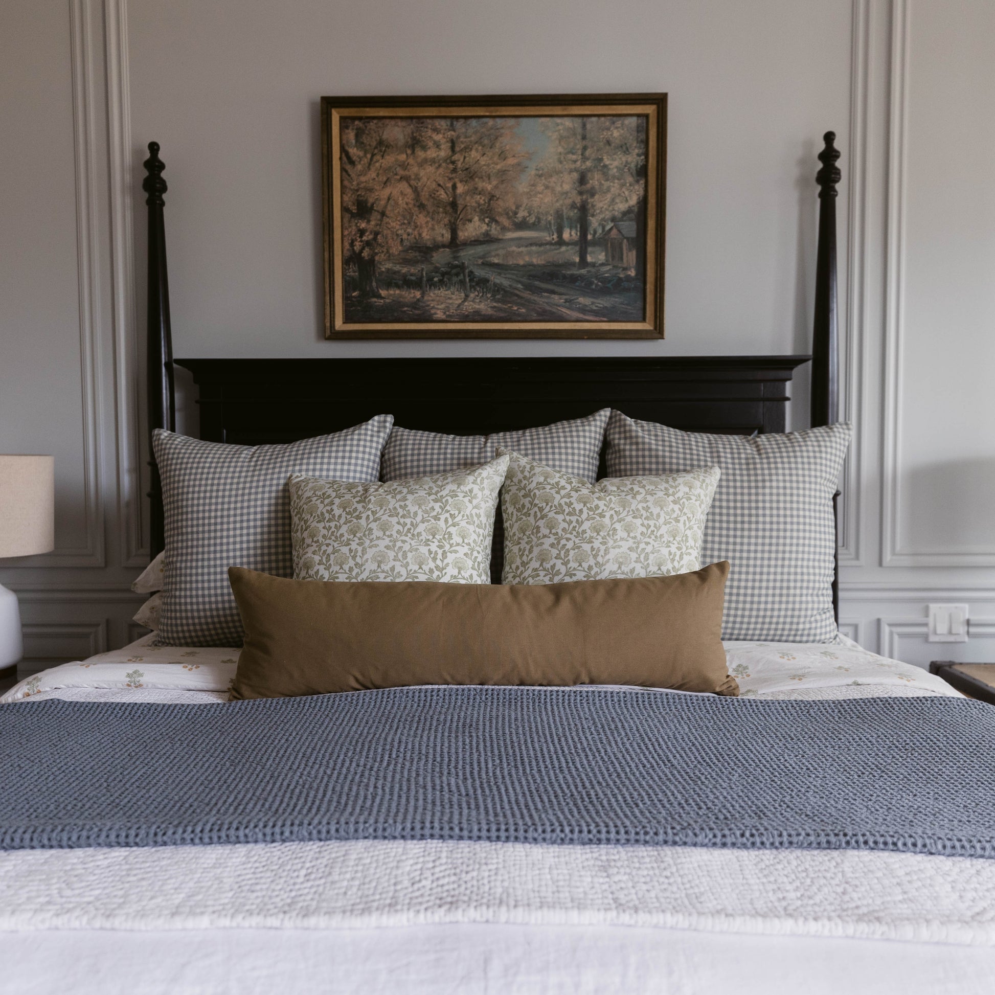 Dusty blue gingham check pillows arranged on a black bed frame with a brown lumbar pillow and blue textured bedding.