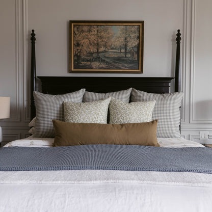 Tan linen lumbar pillow displayed on a black bed with gingham and patterned pillows.