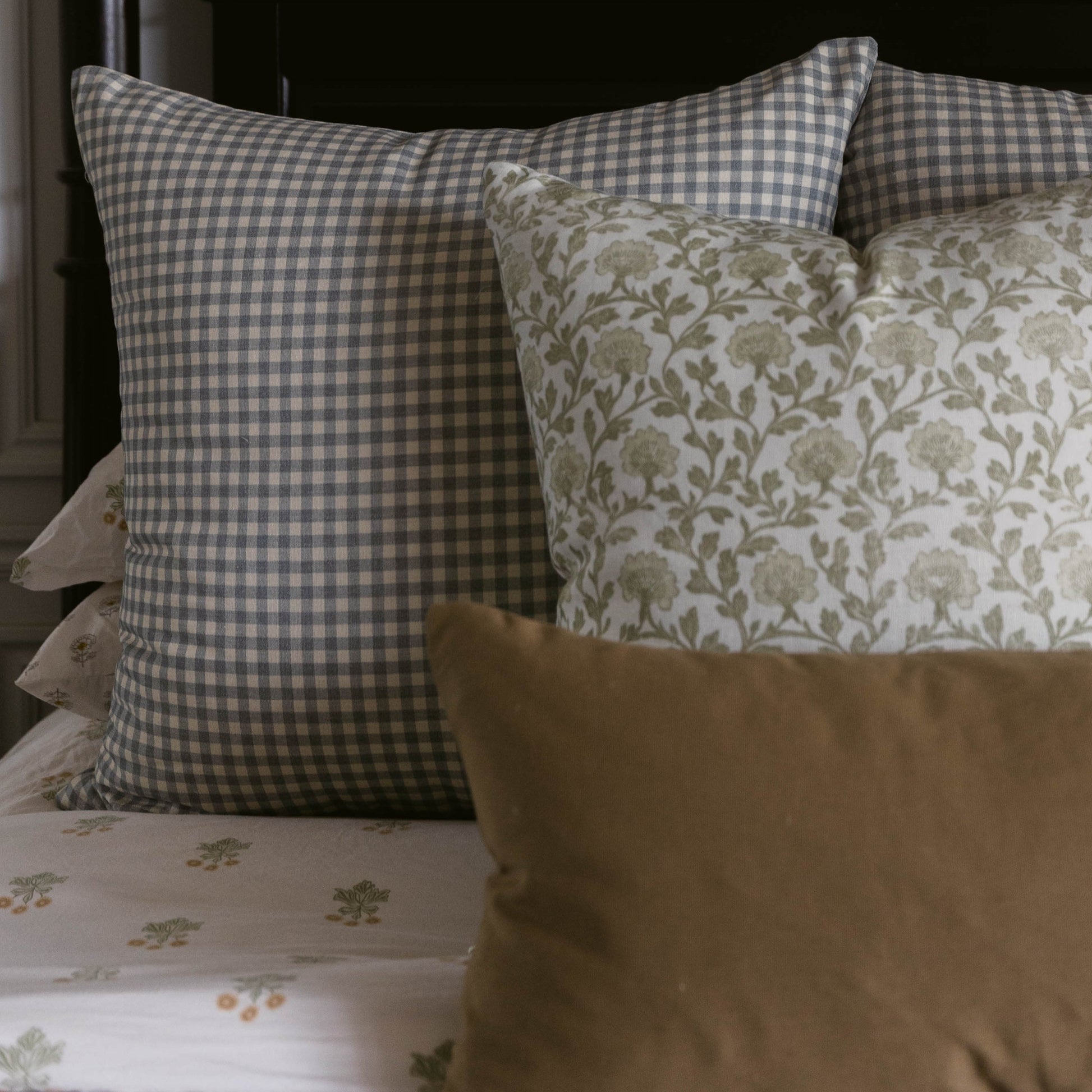 Dusty blue and white gingham checkered pillow displayed on a bed with coordinating patterned pillows.