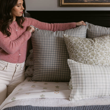 Dusty blue and white gingham check pillow displayed on bed with woman holding corner.