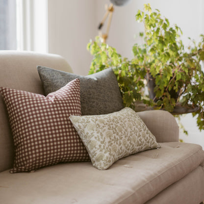 Three decorative pillows in neutral tones with gingham and floral patterns arranged on a beige armchair.