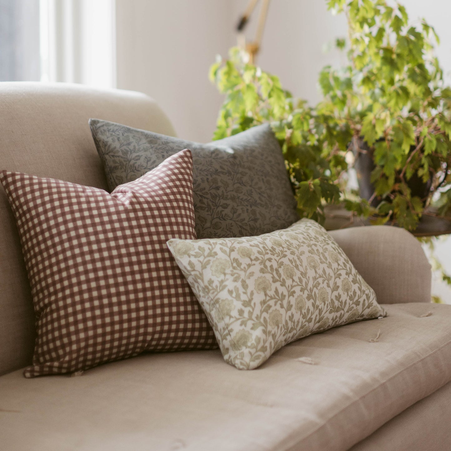 Rose gingham checkered pillow in mauve and white displayed on a cream upholstered chair with coordinating pillows.