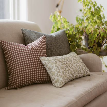 Rose gingham checkered pillow in mauve and white displayed on a cream upholstered chair with coordinating pillows.