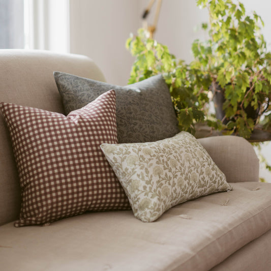 Rose gingham checkered pillow in mauve and white displayed on a cream upholstered chair with coordinating pillows.