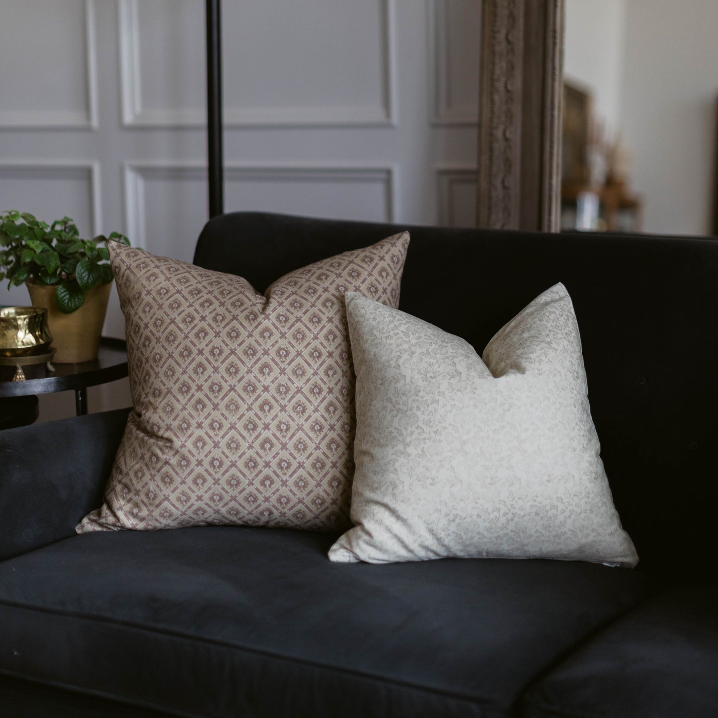 Two decorative pillows on a dark sofa: one with beige geometric diamond pattern, one with light gray solid texture.