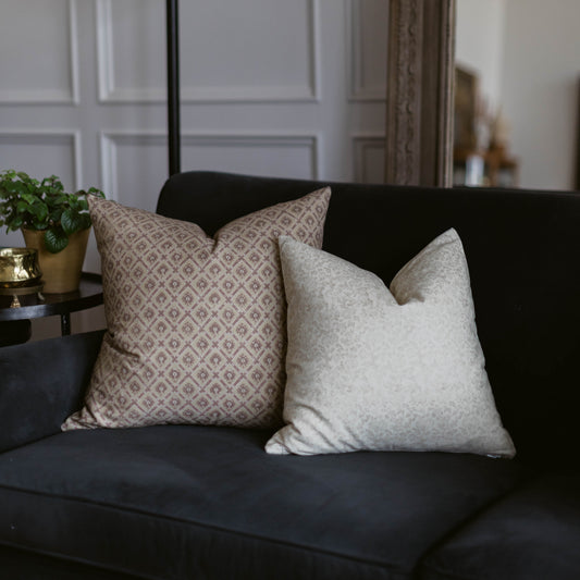 Two decorative pillows on a dark sofa: one with beige geometric diamond pattern, one with light gray solid texture.