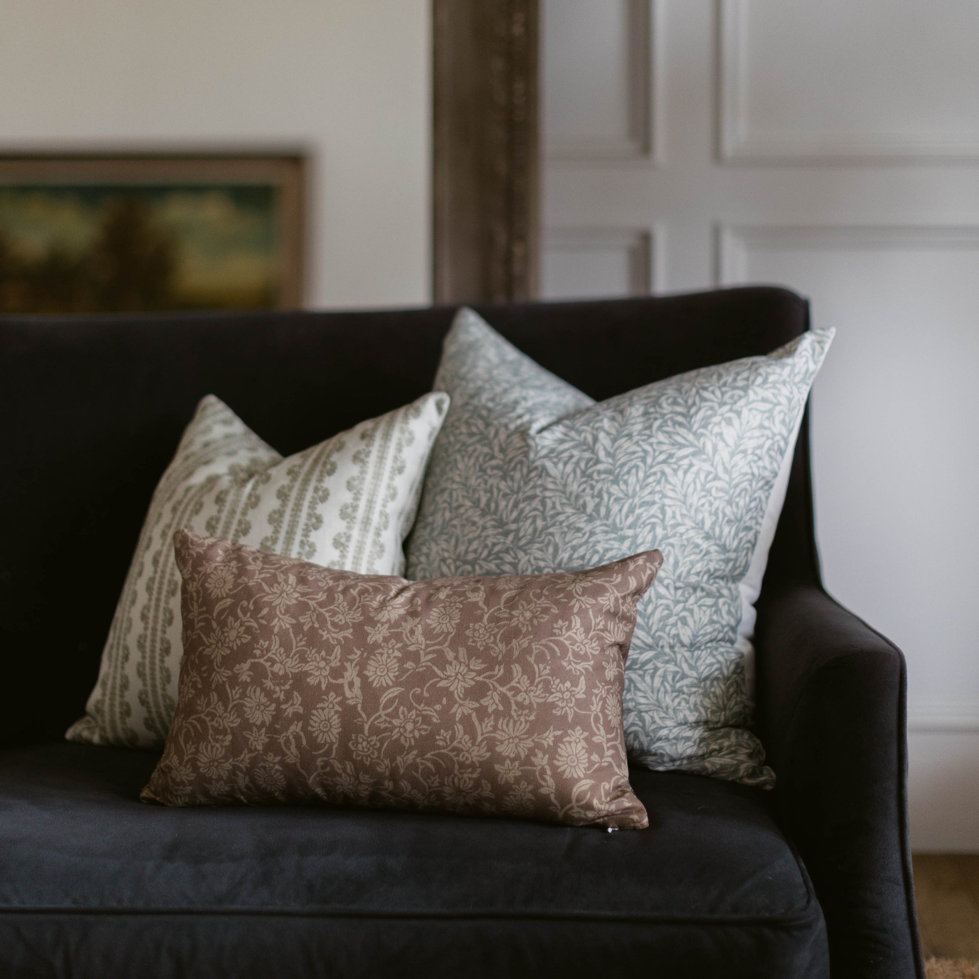 Three decorative pillows with damask and geometric patterns in neutral tones arranged on a black sofa.