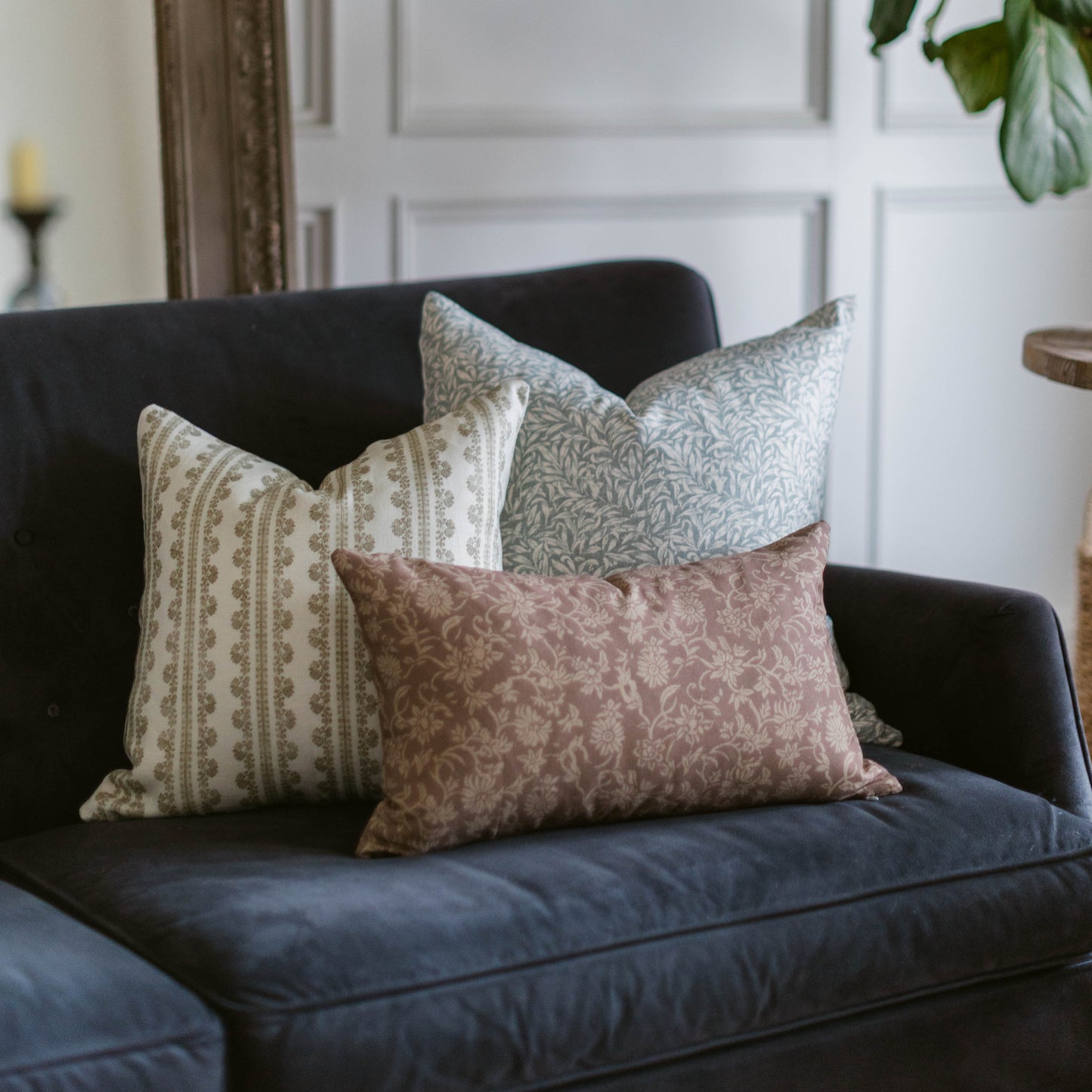 Three linen pillows with geometric and damask patterns in cream, gray, and mauve on a dark sofa.
