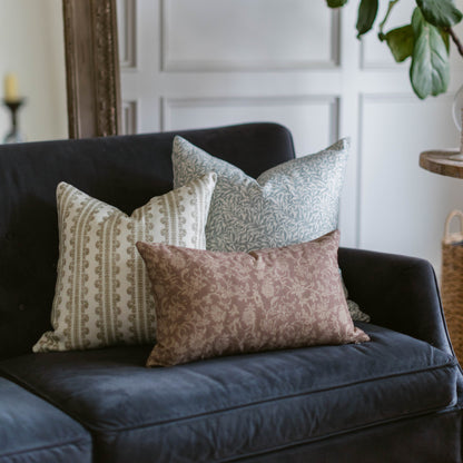 Three decorative pillows with geometric and floral patterns in cream, gray, and mauve on a black upholstered sofa.