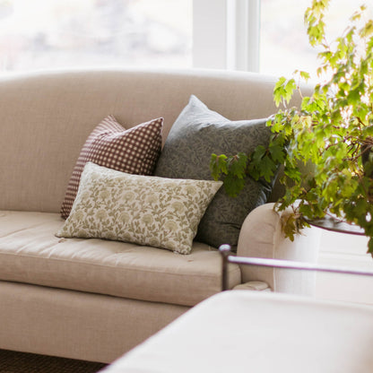 Beige linen pillow with subtle leaf pattern displayed on cream sofa with coordinating decorative pillows near a window.