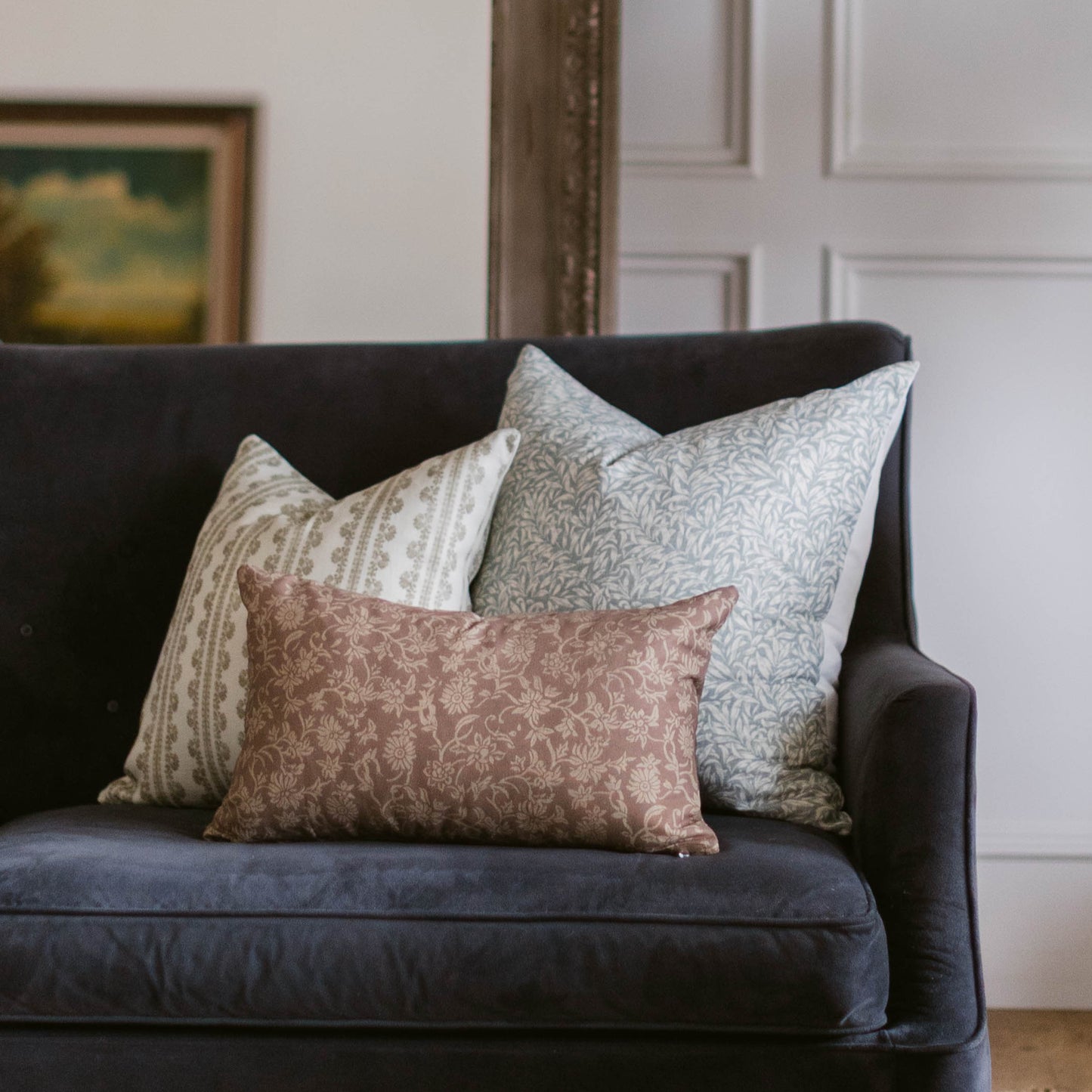 Three decorative linen pillows with reversible designs in cream, gray, and dusty rose floral patterns arranged on a dark sofa