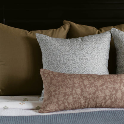 Three linen pillows with damask patterns in gray, taupe, and beige displayed on a bed with tan and blue bedding.