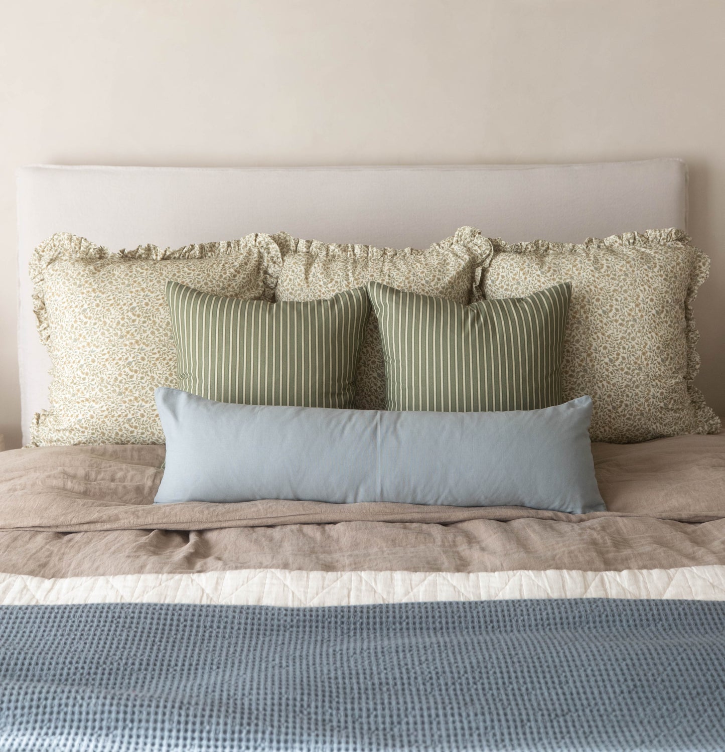 Dusty blue lumbar pillow displayed among coordinating neutral and striped decorative pillows on a bed.