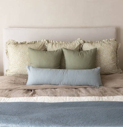 Dusty blue lumbar pillow displayed among coordinating neutral and striped decorative pillows on a bed.