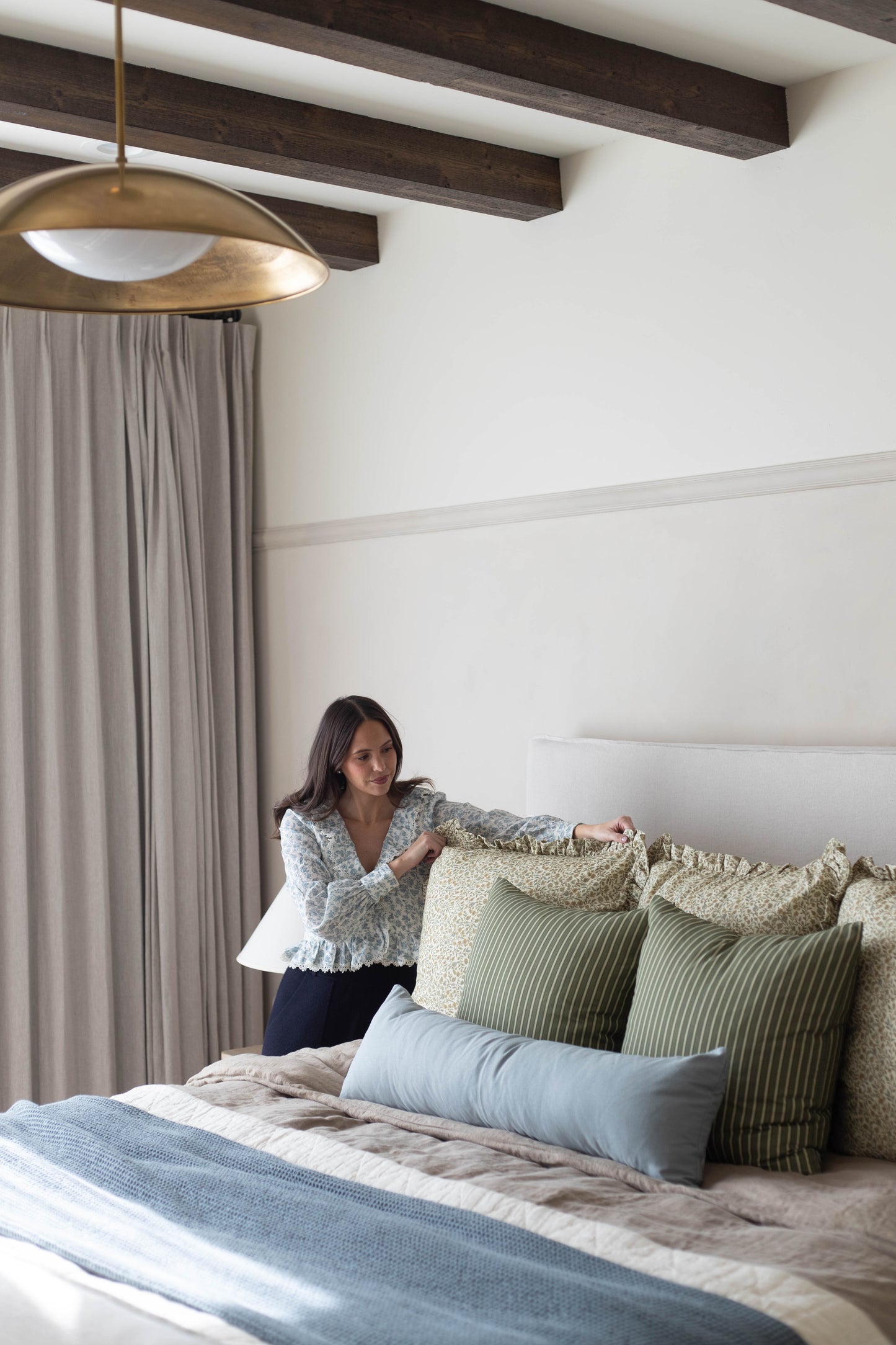 Woman arranging green and cream patterned pillows with ruffled edges on a bed.