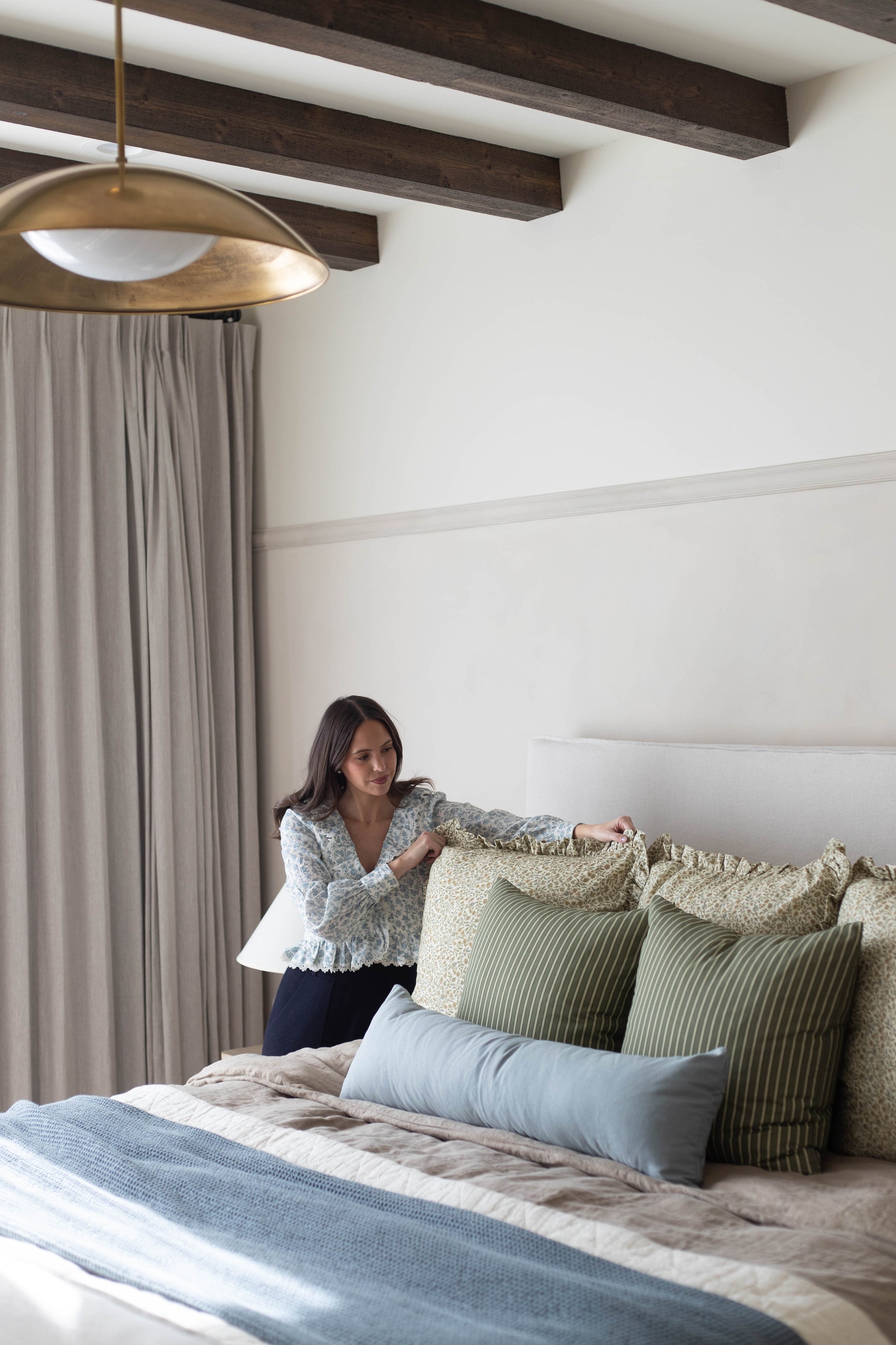 Woman arranging green and cream patterned pillows with ruffled edges on a bed.