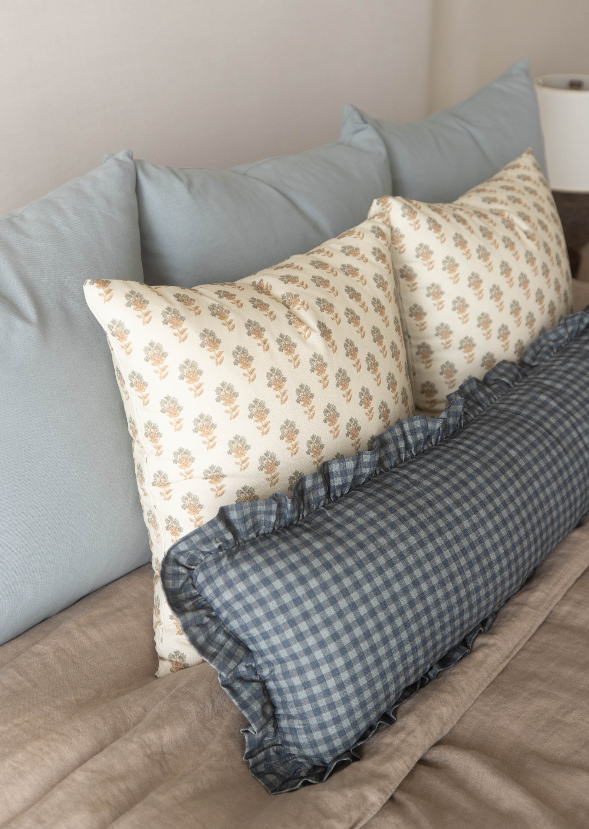 Navy gingham pillow with ruffled edges displayed on a bed with gray pillows.