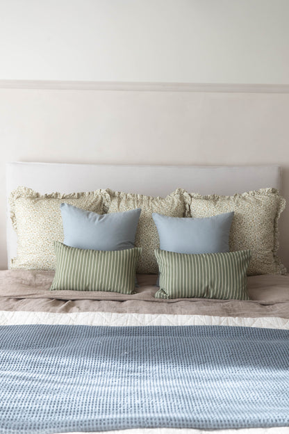 Dusty blue pillow with textured weave fabric displayed on bed with coordinating pillows.