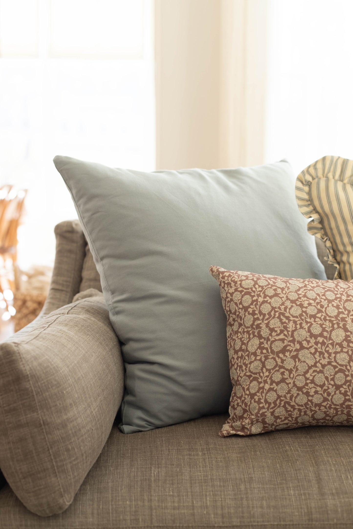Dusty blue solid pillow displayed on a sofa with patterned and neutral accent pillows.