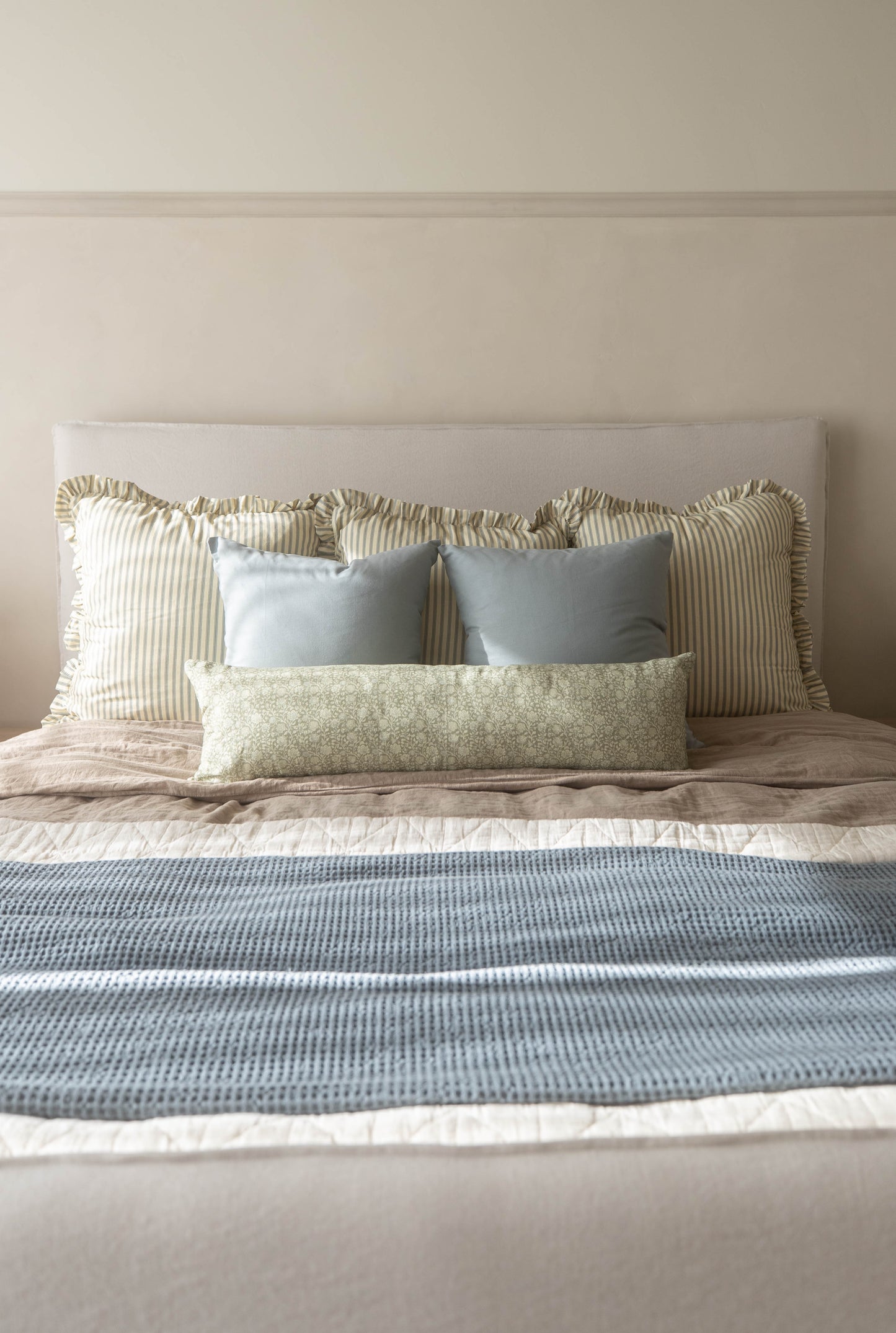 Dusty blue rectangular pillow displayed on a bed with striped and patterned cushions.