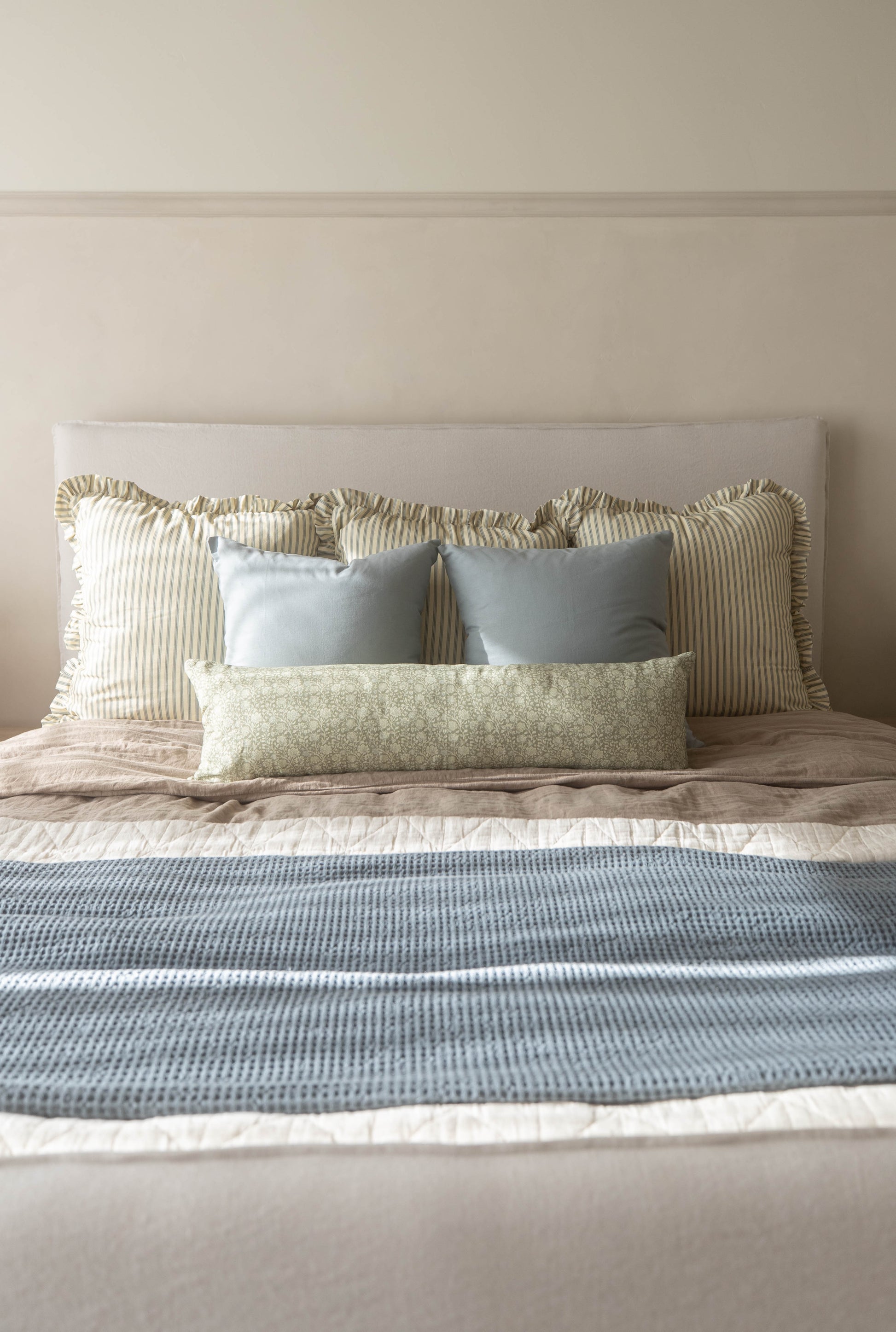 Dusty blue rectangular pillow displayed on a bed with striped and patterned cushions.