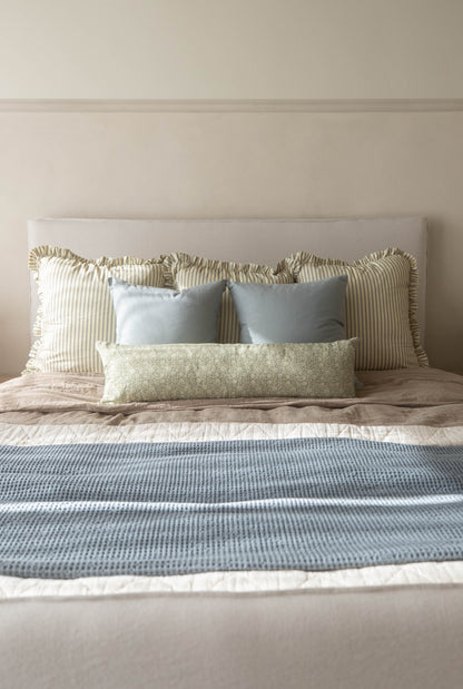 Dusty blue rectangular pillow displayed on a bed with striped and patterned cushions.