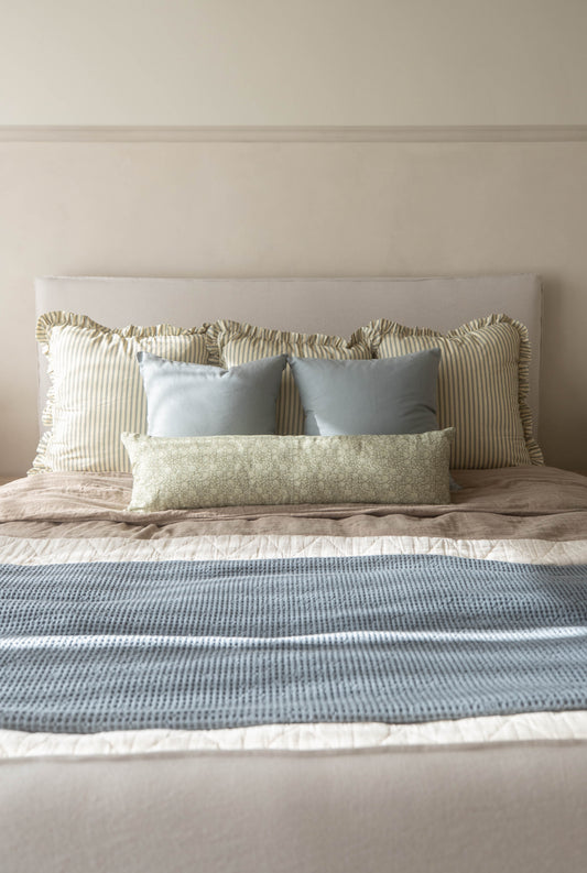 Dusty blue rectangular pillow displayed on a bed with striped and patterned cushions.