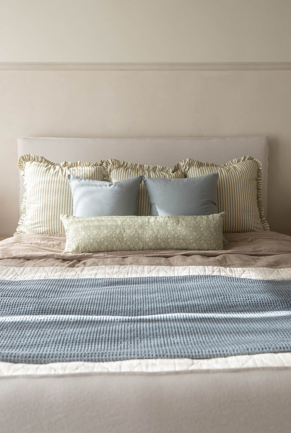 Dusty blue rectangular pillow displayed on a bed with striped and patterned cushions.