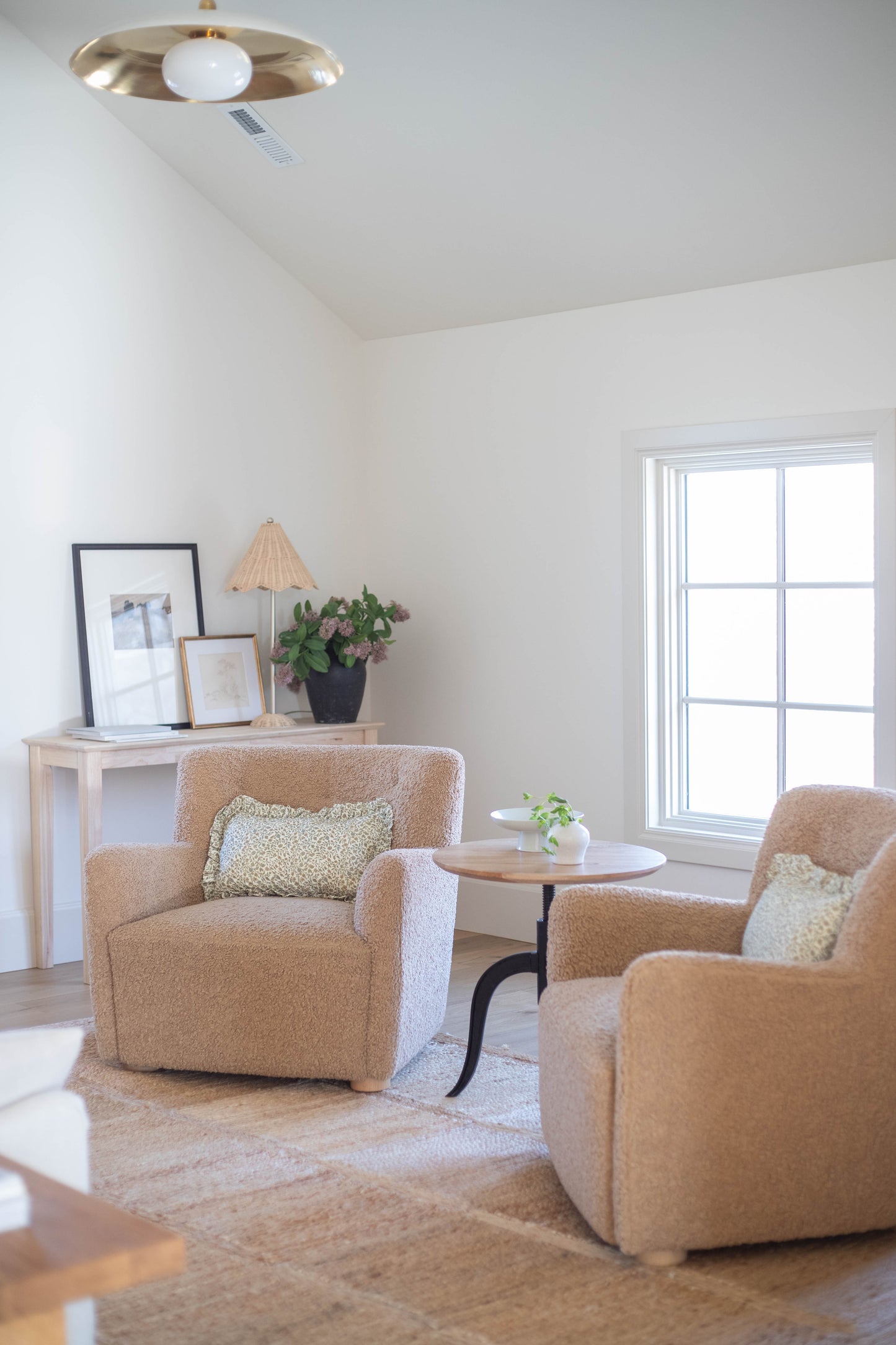 Light brown upholstered armchair with cream pillow in bright living room with pendant light.