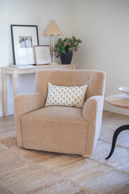 Beige upholstered armchair with curved arms and wooden legs, styled with a patterned cream and tan throw pillow.