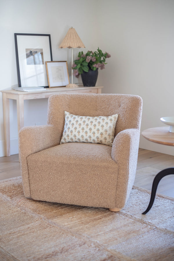 Beige upholstered armchair with curved arms and wooden legs, styled with a patterned cream and tan throw pillow.