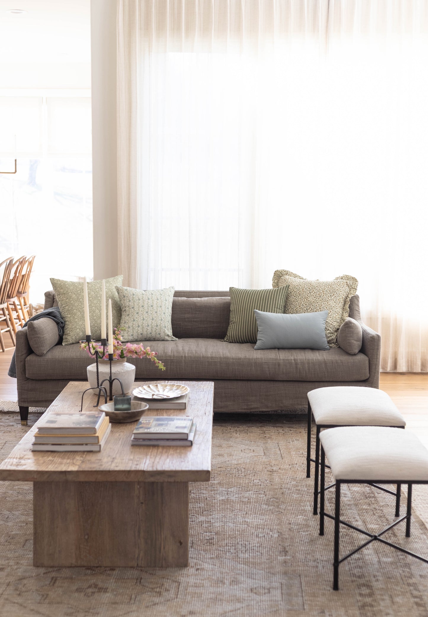 Gray sofa with assorted patterned pillows in green, gray, and blue tones arranged in a bright living room setting.