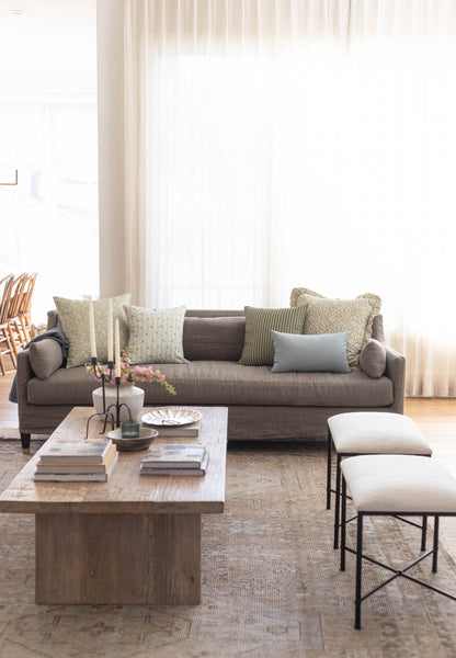 Gray sofa with assorted patterned pillows in green, gray, and blue tones arranged in a bright living room setting.