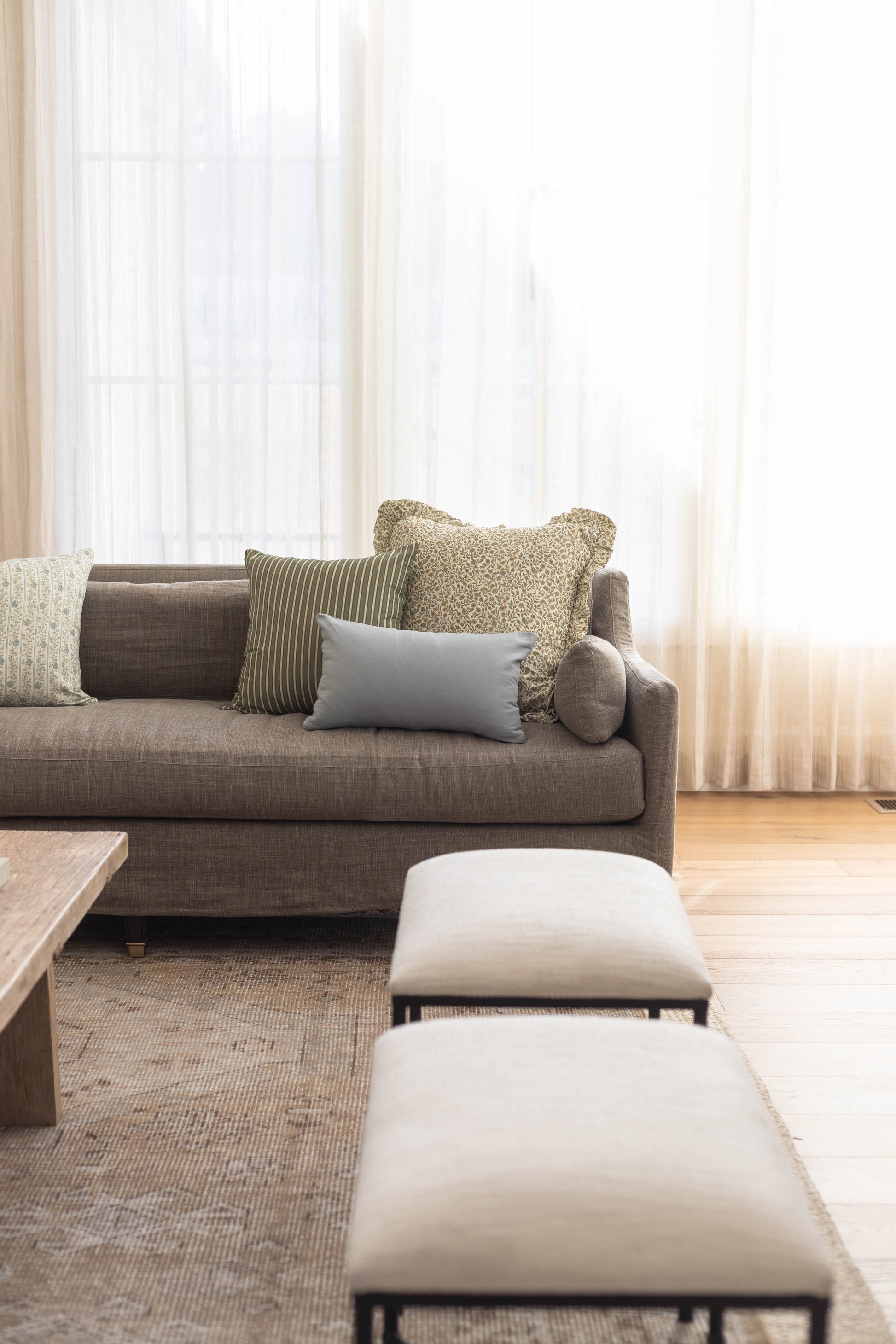 Light gray lumbar pillow displayed on gray sofa with decorative pillows in bright living room setting.