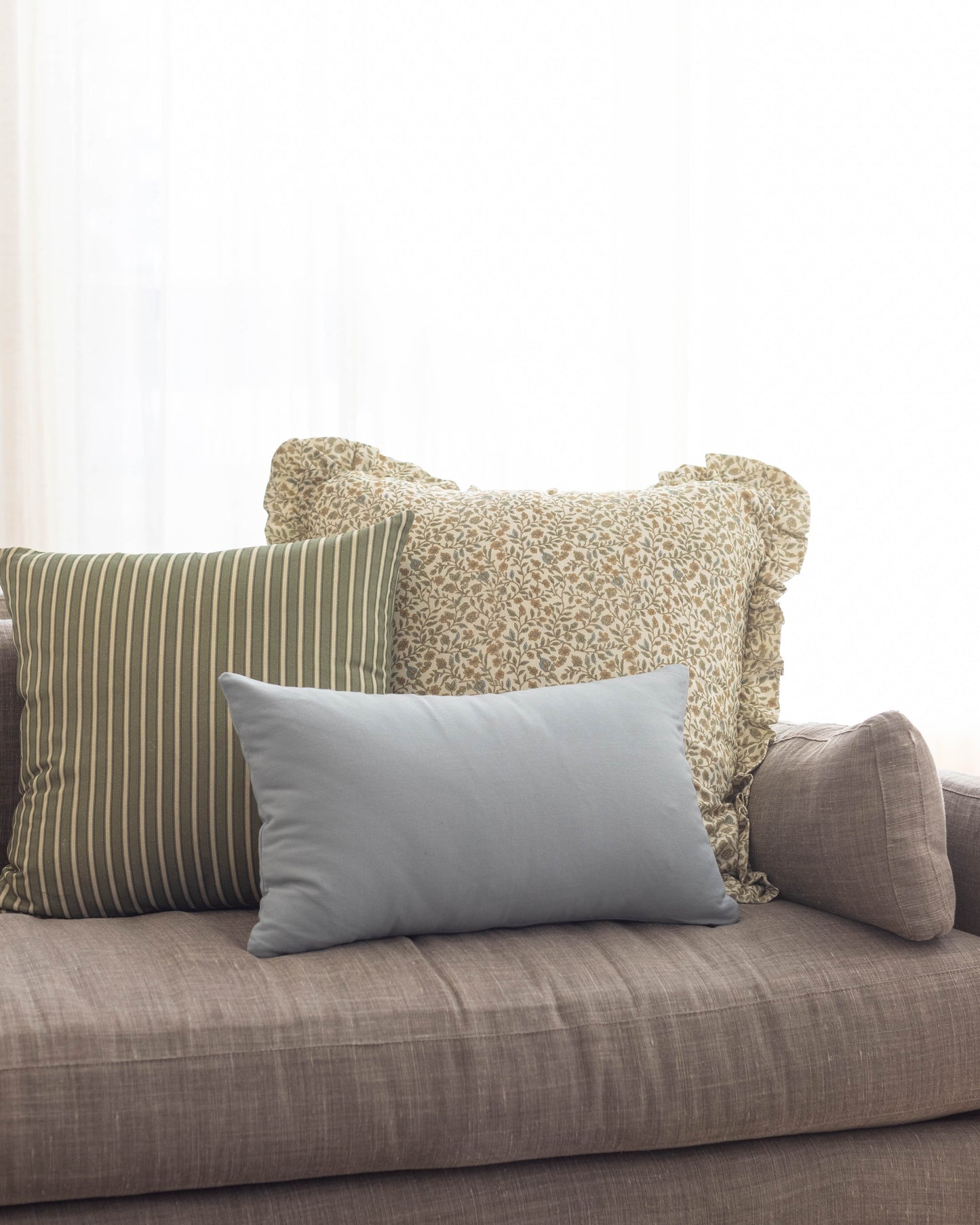 Dusty blue rectangular pillow displayed on a gray upholstered sofa with striped and patterned pillows.