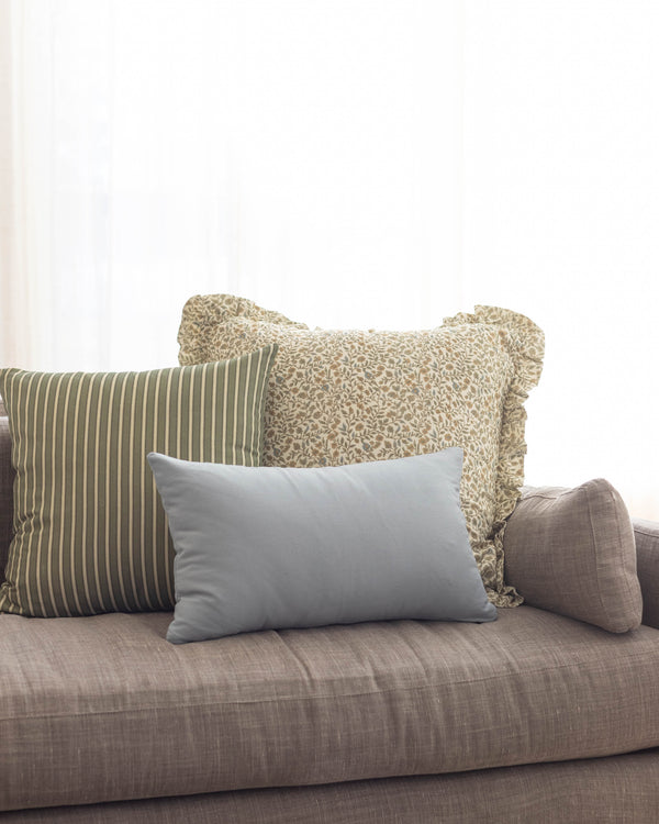 Dusty blue rectangular pillow displayed on a gray upholstered sofa with striped and patterned pillows.