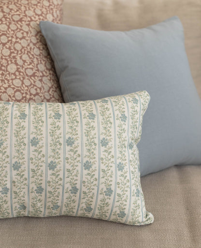 Dusty blue solid pillow displayed with a striped floral patterned pillow on a beige surface.