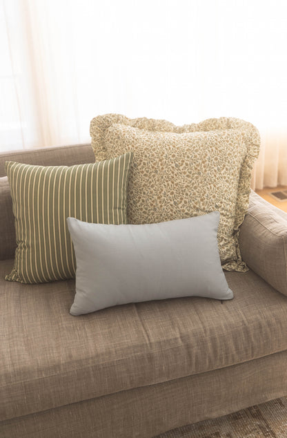 Three throw pillows on a beige sofa: striped green and cream, textured cream with ruffled edges, and solid gray rectangular p