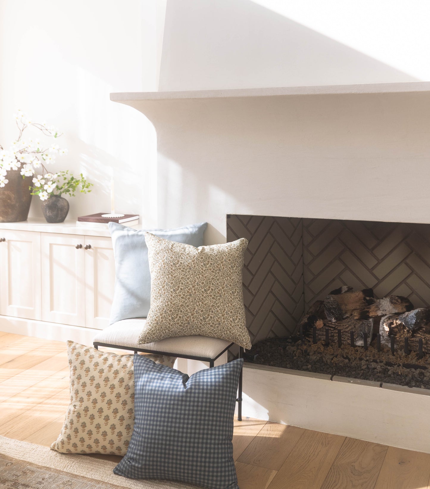 Dusty blue gingham pillow displayed on a stack of patterned pillows in a bright living room setting.