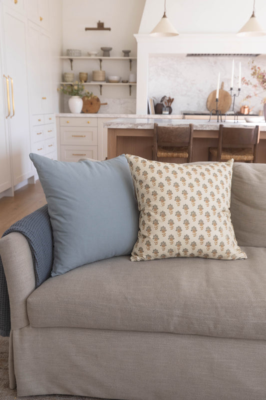 Four decorative pillows in blue, patterned cream, and neutral tones arranged on a beige upholstered sofa.