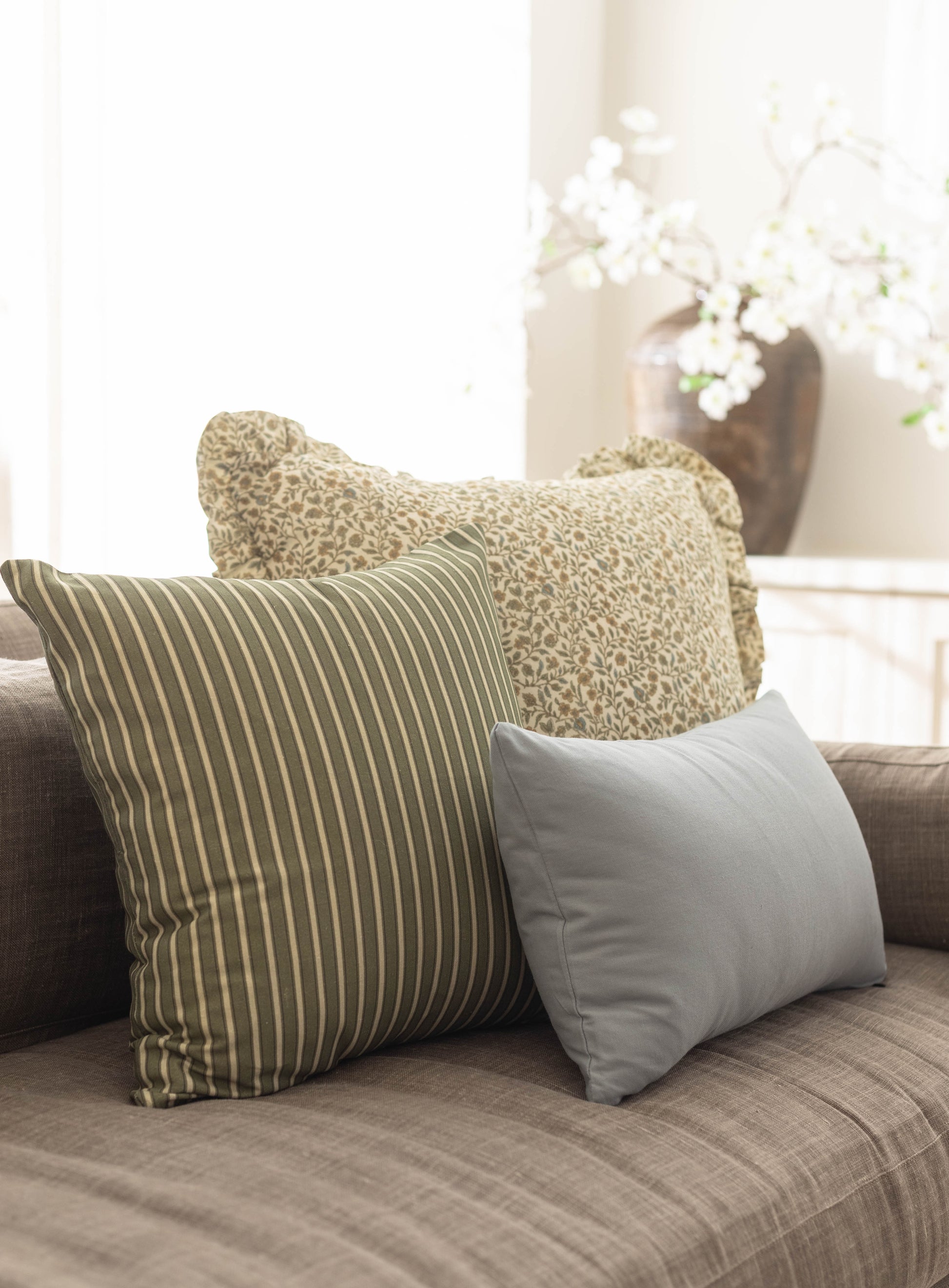 Three decorative pillows in striped and textured fabrics arranged on a gray upholstered sofa.