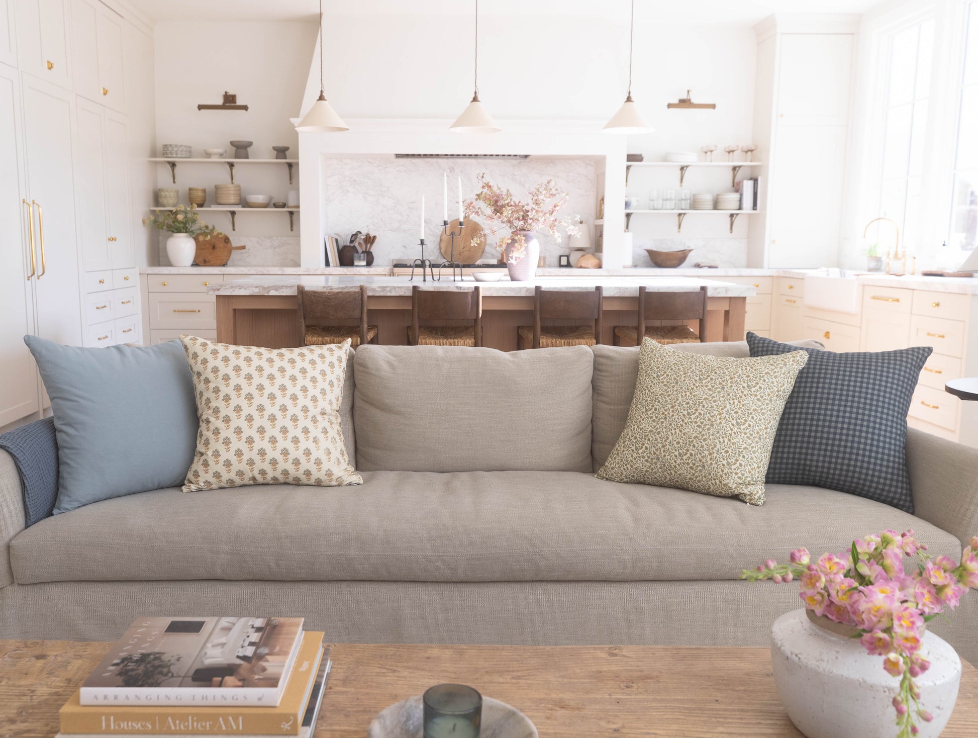 Dusty blue, cream, and gray decorative pillows arranged on a beige sofa in a bright kitchen and living room setting.
