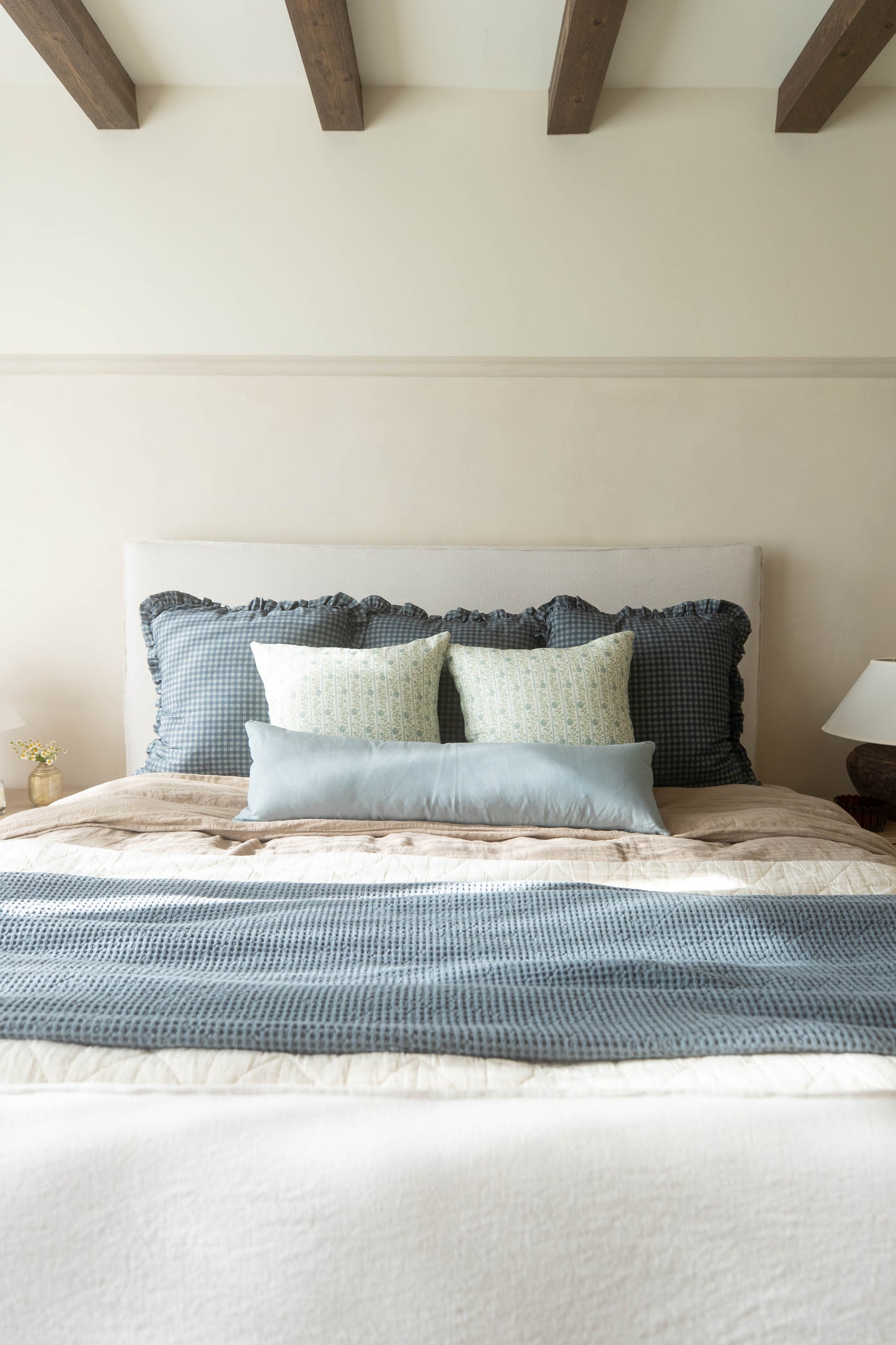Navy gingham ruffle pillow with wavy edge detail displayed on a bedroom bed.