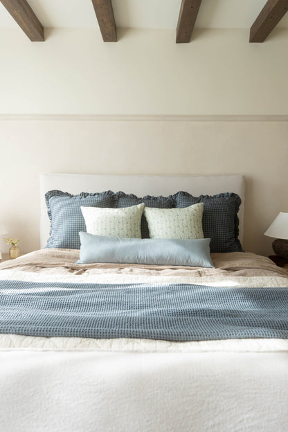 Navy gingham ruffle pillow with wavy edge detail displayed on a bedroom bed.