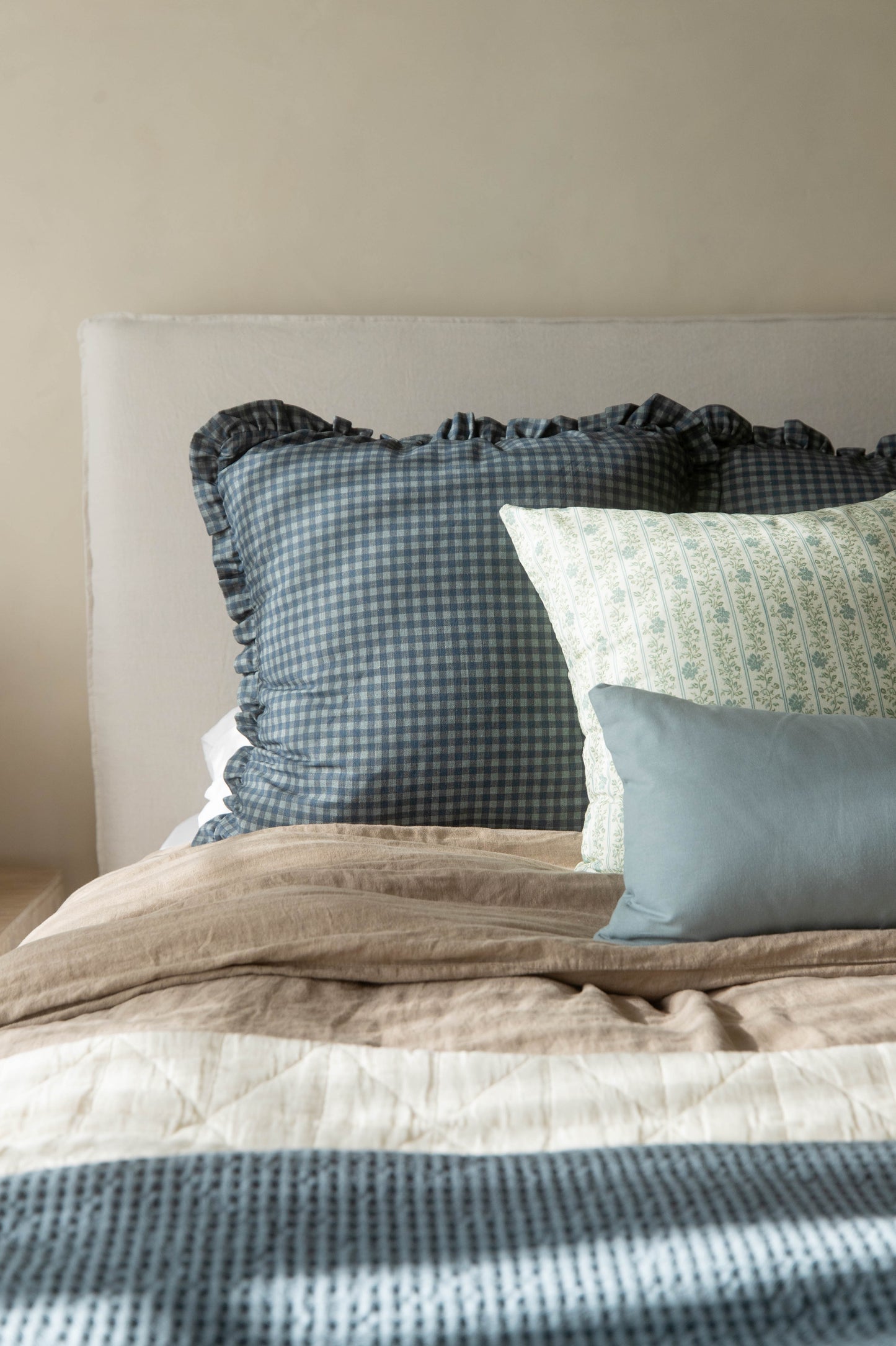 Navy gingham pillow with ruffled edges displayed on a bed with coordinating pillows and bedding.