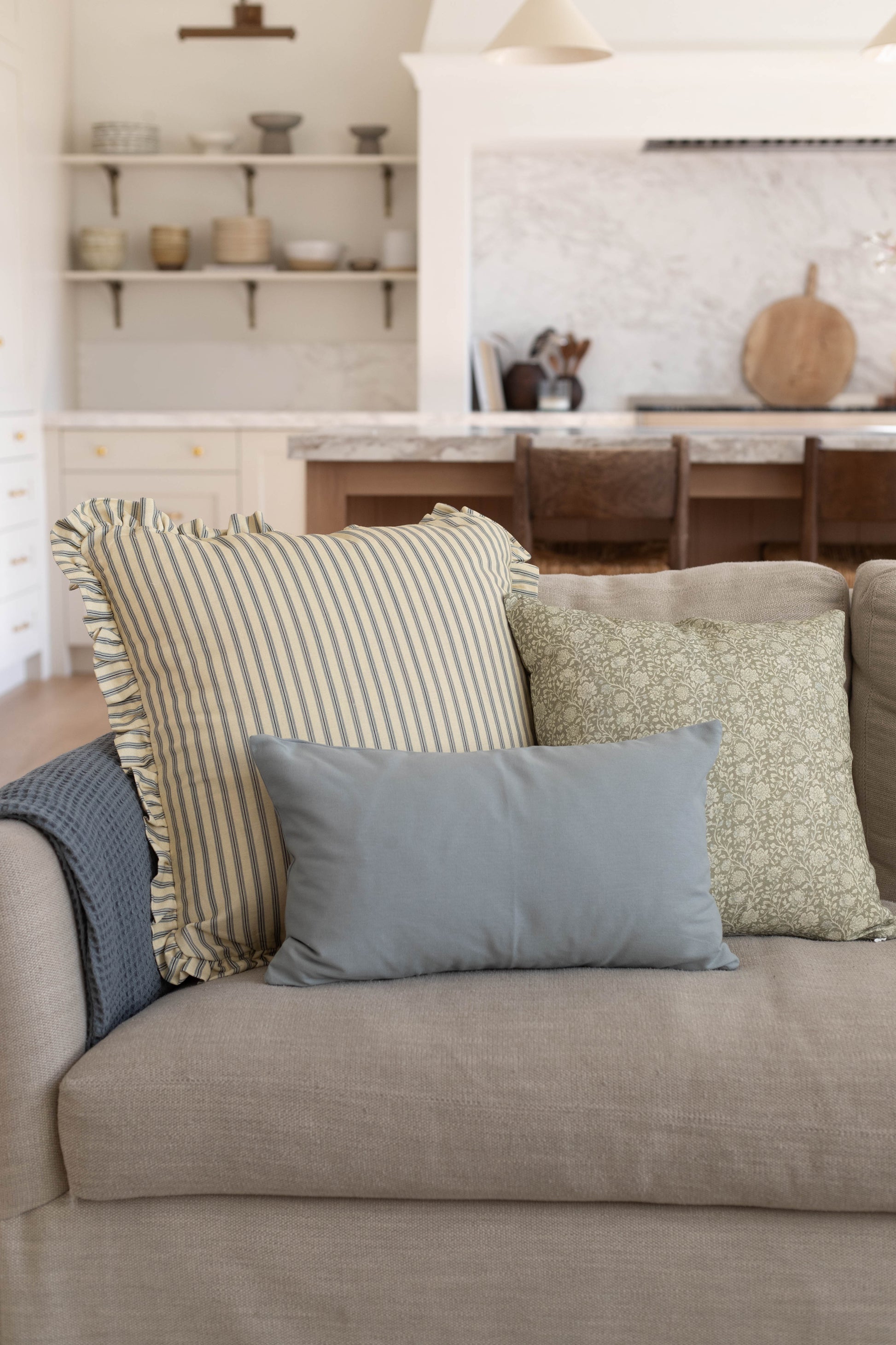 Dusty blue solid lumbar pillow displayed on beige sofa with striped and patterned pillows.