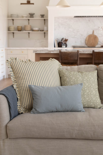Dusty blue solid lumbar pillow displayed on beige sofa with striped and patterned pillows.
