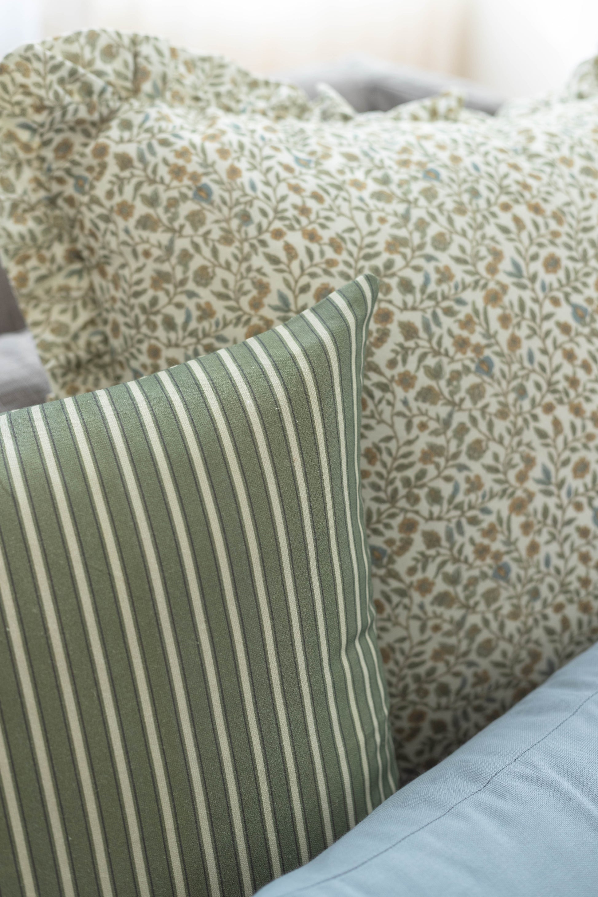 Green and cream striped pillow in foreground with floral patterned pillows behind it on bed.